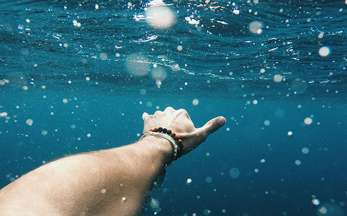 Ragazzo immerso in acqua fa con la mano il saluto dei surfisti (hang loose)